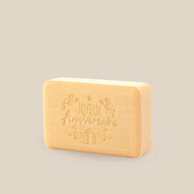 Photo produit prise de côté : Savonnette marseillaise au beurre de karité, de couleur orangée pâle, estampillée Joyeux Anniversaire avec confettis, cadeaux et ballons de fête. Fabriqué à Marseille. 125g.