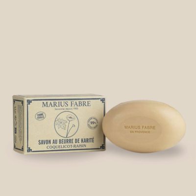 Photo produit : Savon ovale de couleur beige au beurre de karité et à l'huile d'amande douce, parfumé coquelicot-raisin, vient dans une boîte recyclée.