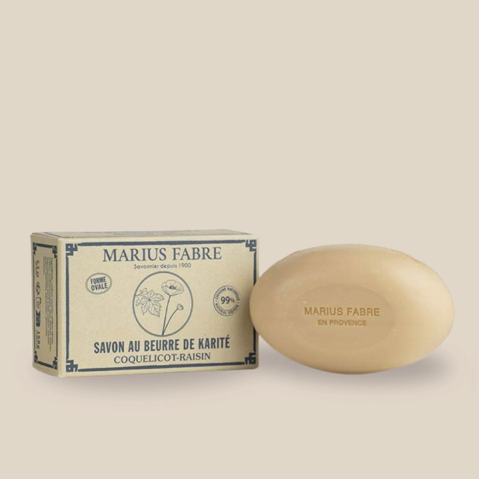 Photo produit : Savon ovale de couleur beige au beurre de karité et à l'huile d'amande douce, parfumé coquelicot-raisin, vient dans une boîte recyclée.